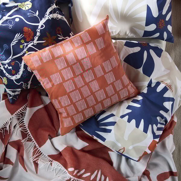 Colorful cushions with patterns, including smaller orange grid design, on patterned fabric.