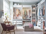 Walk-in closet with white PAX wardrobes, chest, chairs, and flowers.