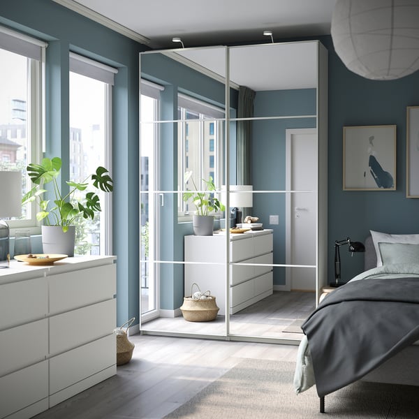 Modern bedroom with teal walls, white PAX wardrobe, gray bed, and green plants.