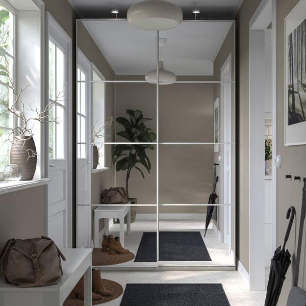 Modern entryway with PAX wardrobe, mirror doors, grey rug, brown boots, beige bag, and hanging plants.