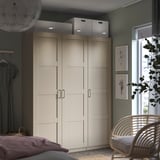 Modern bedroom with beige PAX wardrobe, double doors, built-in lights, hanging rack, dark green walls, chair, art prints.