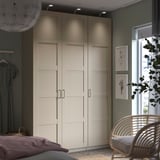 Modern bedroom featuring PAX wardrobe in beige, with a wicker chair, gray walls, and natural light.