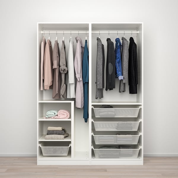 A white PAX wardrobe with sliding doors displays clothes on hangers and shelves. Baskets store folded items.