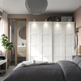 A modern bedroom a white PAX wardrobe, neatly made bed with grey linens, and a sleek mirror.