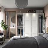 Modern bedroom with white PAX wardrobes, soft lighting, grey bed, and plant - minimalist design.