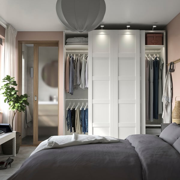 A modern, minimalist bedroom featuring a white PAX wardrobe with sliding doors, housing clothes and shelves.