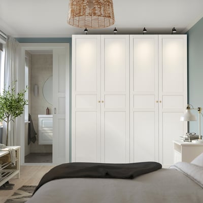 Modern bedroom with large PAX wardrobe, cosy bed, side table lamp, and door to minimalistic bathroom.