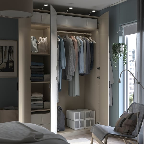 Modern bedroom featuring a PAX wardrobe with organized clothes, shelves, mirrors, and white decor.