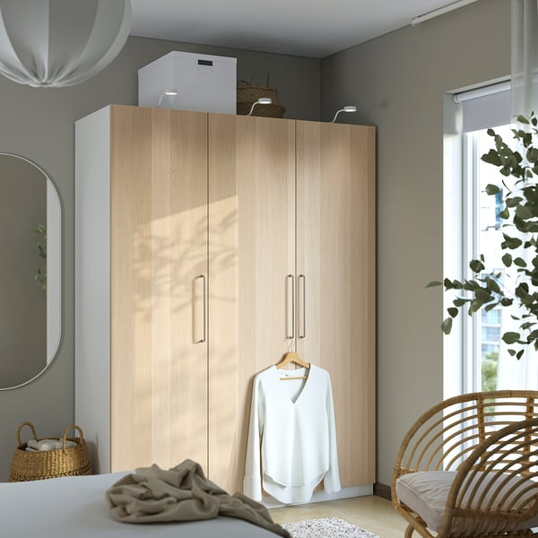 Modern bedroom with PAX wardrobe, clothes, wicker chair, plants, and mirror.