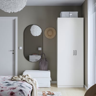 Modern bedroom with white PAX wardrobe, round mirror, and floral bedding against a dark wall.