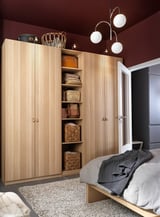 Bedroom with light wood PAX wardrobe, open shelving showing woven baskets, hanging lights, gray bedding on bed, gray rug, maroon walls.