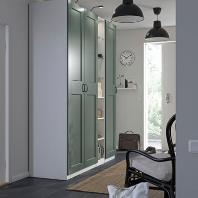 Sage green PAX wardrobe in hallway, with shelves, black handles, rocker chair, clock, and lights.