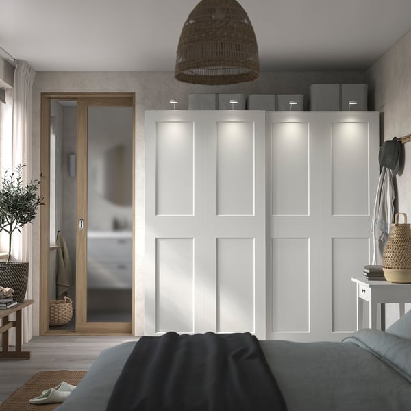 A modern, minimalist bedroom with a white PAX wardrobe, sliding doors, and gray bedding.