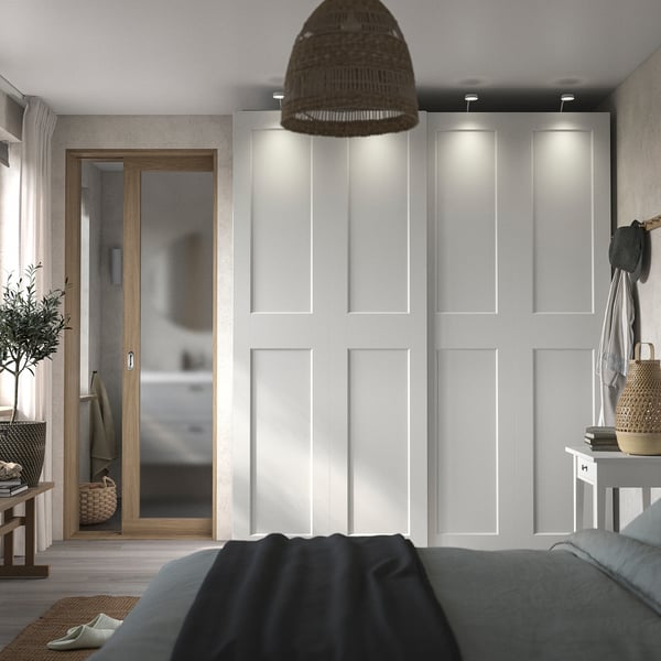Bedroom with PAX wardrobe, mirror, grey blankets, wooden elements, and a wicker hanging lamp.