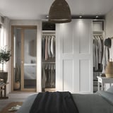 Modern bedroom with gray bed, open closet showing clothes, wicker lights, and a white sliding mirror door.