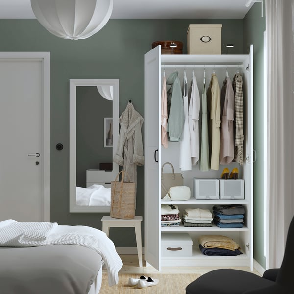 Bedroom with PAX wardrobe displaying clothes, folded items, & storage, beside a mirror and bed.