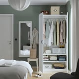 Bedroom with PAX wardrobe displaying clothes, folded items, & storage, beside a mirror and bed.