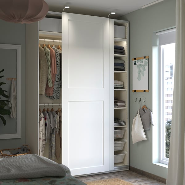 A modern white PAX wardrobe organizes clothes and accessories in a neatly arranged nursery. It sliding doors, shelves, and hanging racks.