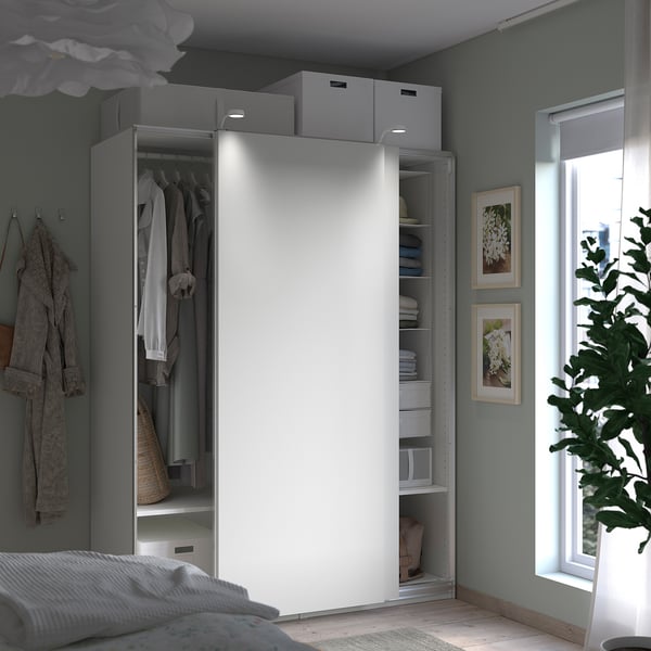 Modern bedroom with a white PAX wardrobe featuring sliding doors, hanging clothes, shelves, and storage boxes.