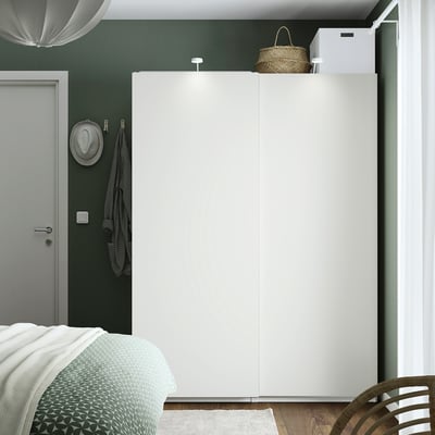 Minimalist bedroom with tall white PAX wardrobe against dark green wall, next to gray door.