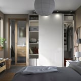Modern bedroom with white PAX wardrobe, sliding doors, open shelves, gray bed, and wooden bench.