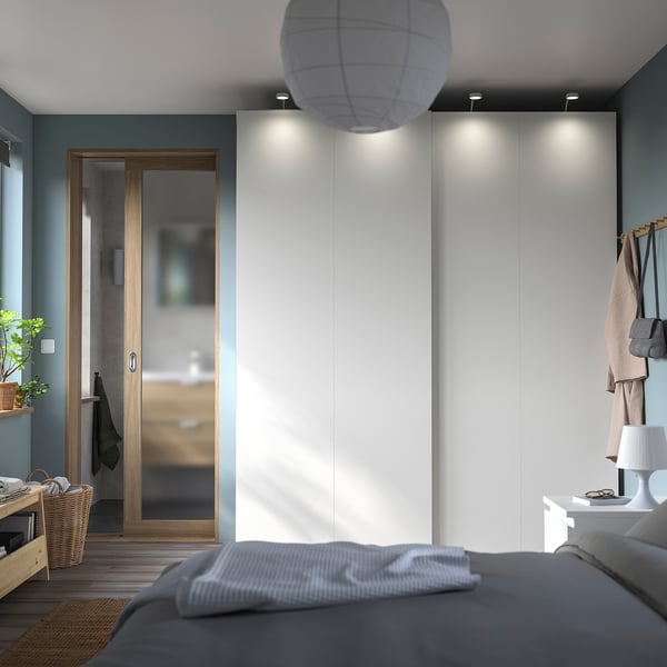 Modern bedroom with gray bed, white wardrobe, wooden door, pendant light, and nightstand with lamp.