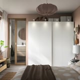 Modern bedroom with white PAX wardrobe, mirrored closet doors, beige polka dot bedding, hanging lantern, and potted plant.