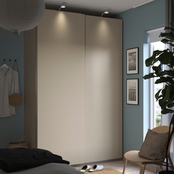 Modern bedroom with light grey PAX wardrobe, plants, black bedding, striped shirt, and wooden chair.