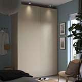 Modern bedroom with light grey PAX wardrobe, plants, black bedding, striped shirt, and wooden chair.
