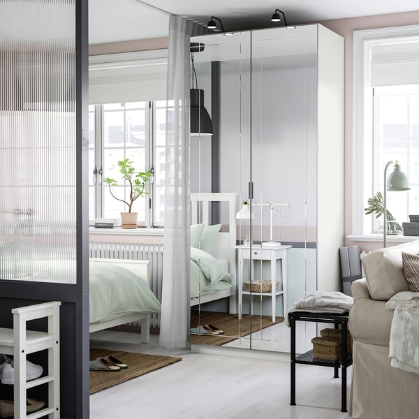 Modern bedroom with white PAX wardrobe featuring mirrored doors, reflecting light.