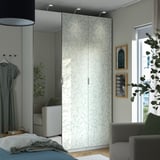 Modern bedroom with white PAX wardrobe, sleek dresser, cozy chair, stylish floral design.