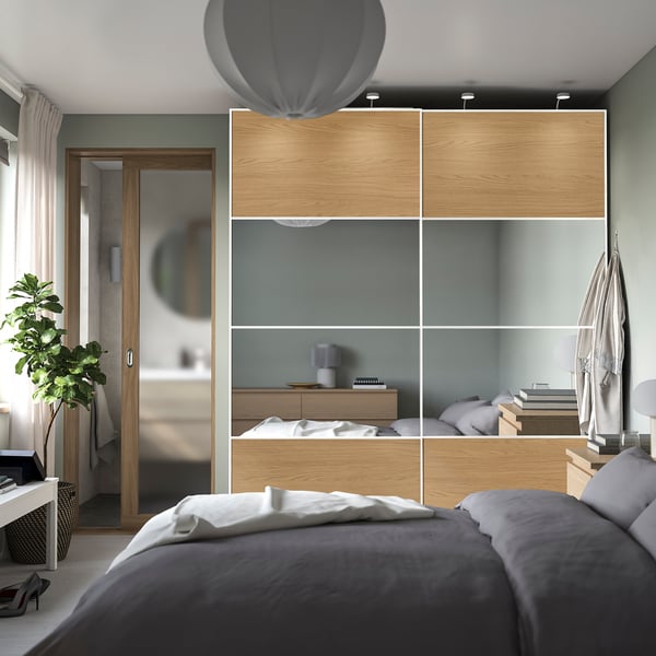 Modern bedroom with PAX wardrobe, sliding doors, glass panels. Grey bed, pendant light, plant. Bathroom with round mirror through open door.
