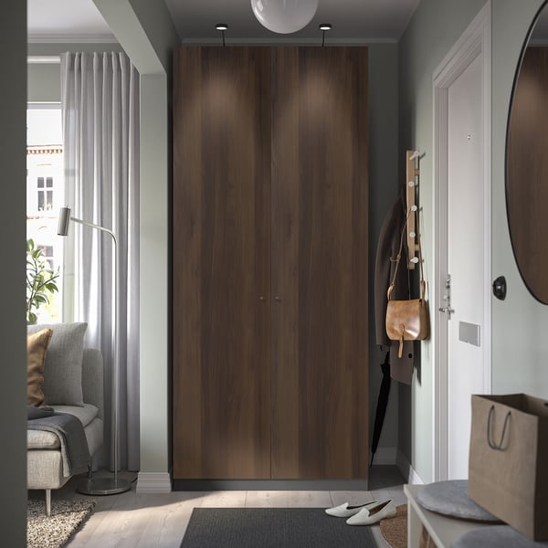 Modern entryway with tall brown PAX wardrobe, white door, grey chairs, and tan accessories. Wardrobe is massive compared to other items.