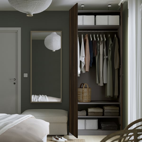 A modern bedroom with a PAX wardrobe open, displaying clothes and storage boxes inside. A mirror, bed, and pendant lights are visible.