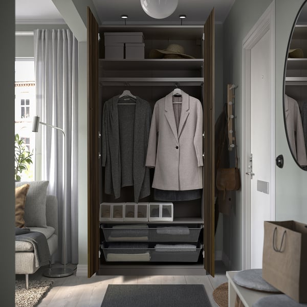 Closed wardrobe named PAX shown open, displaying hangers, shelves, and storage bins inside a stylish, narrow frame.