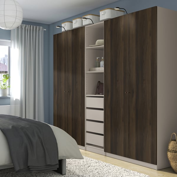 Modern bedroom with dark brown PAX wardrobe. Includes shelves, drawers, and baskets. Beside bed and window with blue curtains.