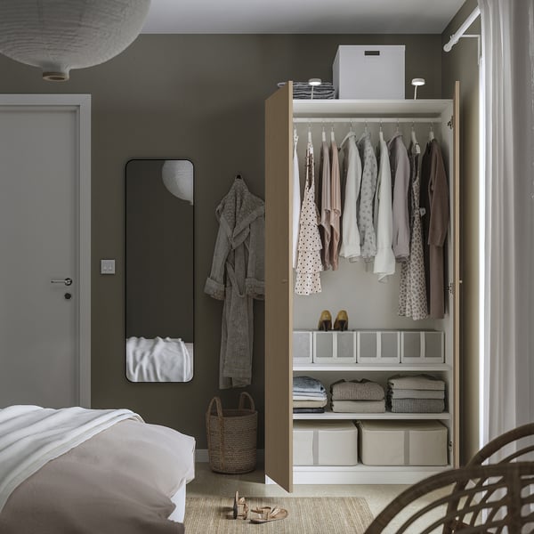 Bedroom with open wardrobe showing clothes and storage boxes; includes mirror, robe hook, and basket.