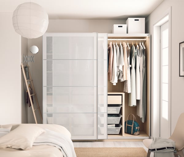 Modern bedroom with white sliding closet, clothes, handbag, ladder, white decor, and bed with white linens.