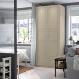 Modern studio with beige PAX wardrobe, tall and narrow, beside grey sofa. Soft lighting, minimalist decor.