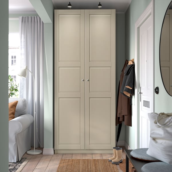 Modern entryway with tall wardrobe, coat hooks, and small rug. Wardrobe flanked by sofa and mirror, light wooden floor, soft curtains.
