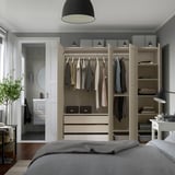 Modern bedroom with built-in wardrobe, clothes hangers, shelves, and drawers for organized storage. Grey-beige color scheme.