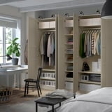 Bedroom with an open beige PAX wardrobe showing clothes, shelves, and organized storage.