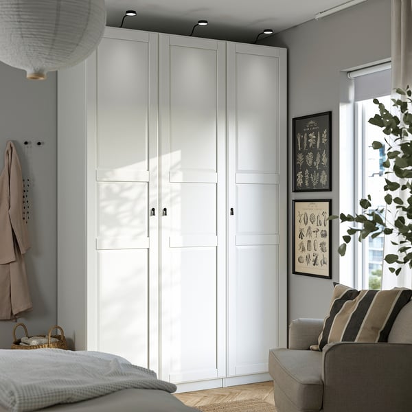 A white PAX wardrobe set, corner-spanning with soft-close doors and drawers, complementing a minimalist room.