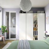 Modern bedroom with PAX wardrobe, spherical light, green bed linens, glass door, plant.