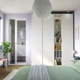 Modern bedroom with tall PAX wardrobe, decorative shelves, glass-door closet, mint-green bed, and pendant light.