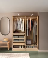 An open wooden PAX wardrobe displays neatly organized clothes and accessories. Light and airy, it glass organizers and drawners for storage.