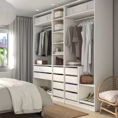 Modern bedroom with a large white PAX wardrobe, featuring shelves, drawers, and hanging space, complementing a bed and wicker chair.