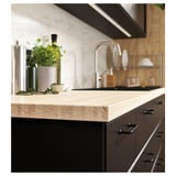 Modern kitchen with black cabinets, light wood countertop, stainless sink, pots, and fresh herbs.