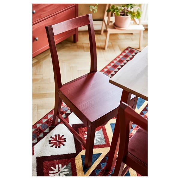 Red wood dining chairs and table setup on colorful rug.