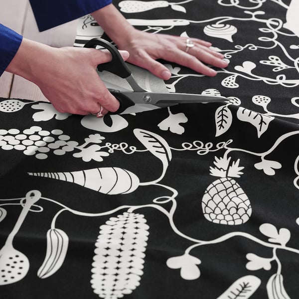 A person cuts a pre-cut fabric featuring a playful, black and white food pattern, ideal for sewing projects like aprons, curtains, or crafts.